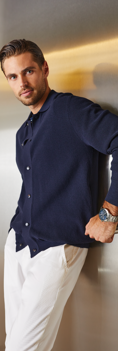 Man wearing a navy blue shirt and white pants against a neutral background