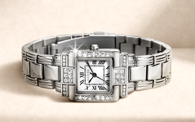 A silver-toned rectangular analog watch with a metal link bracelet, crystal-accented bezel, and a white dial with black Roman numerals, shown on a soft beige background.