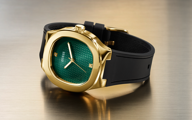 Gold watch with green face and black strap on a reflective surface