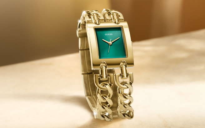 Gold chain-link watch with a green face on a beige surface