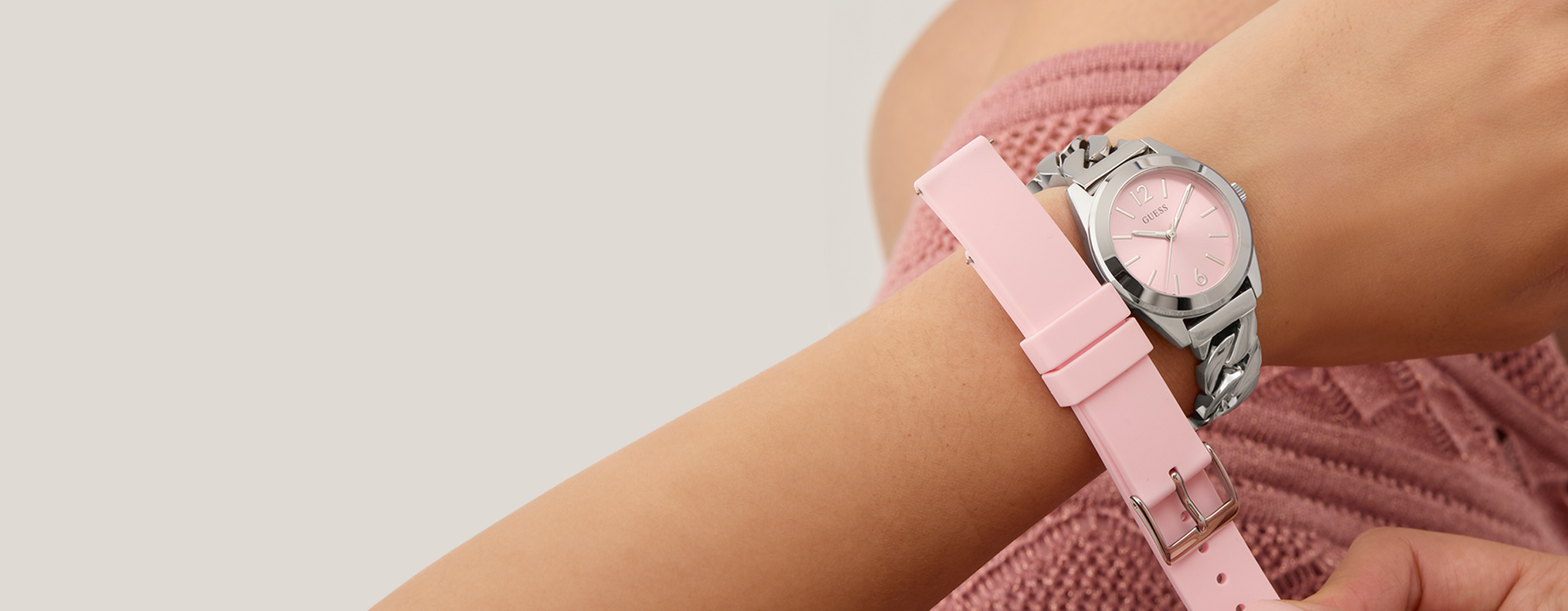 Womans wrist wearing silver watch with pink dial and holding pink silicone extra strap