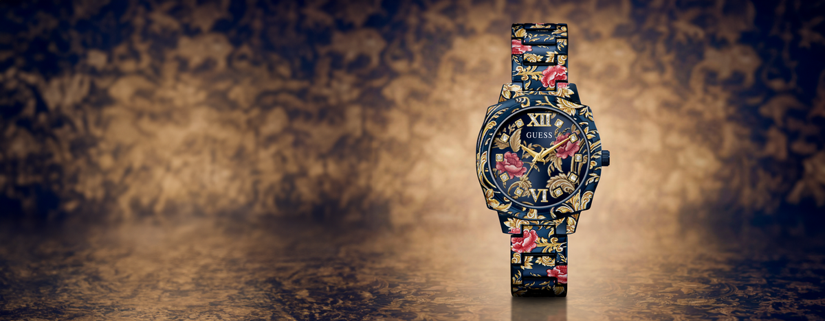 A wristwatch with a dark blue base and a vibrant floral print in pink, red, and yellow, standing upright against a moody, textured background.