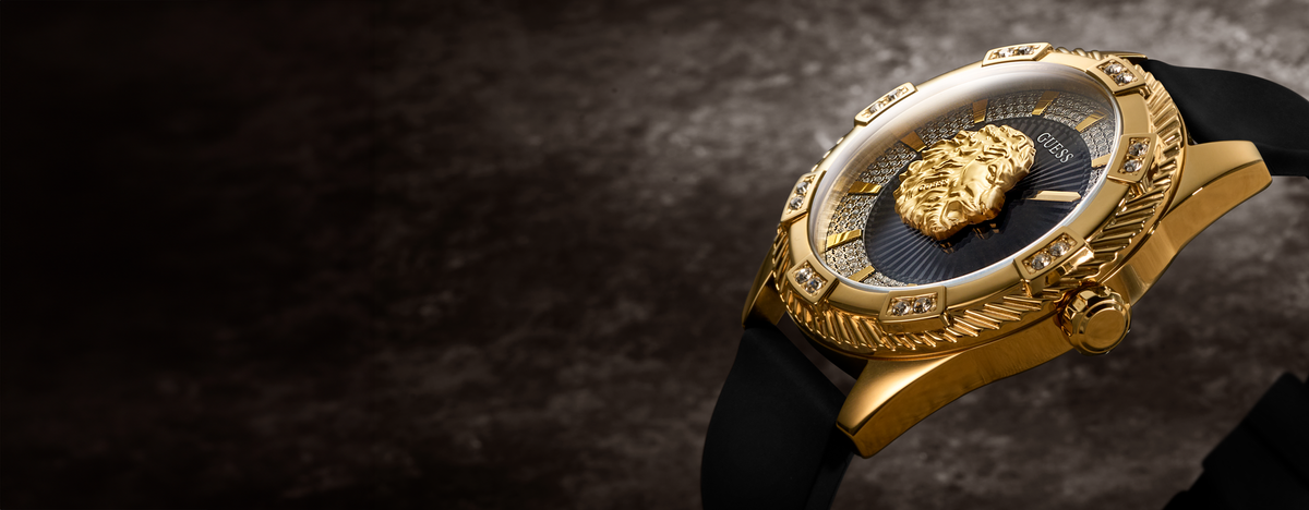A luxury gold-tone watch with a black dial, a prominent lion head emblem on the dial, and a black strap, shown on a dark textured background.