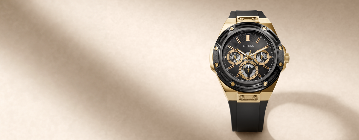 A luxury wristwatch with a gold-tone case, black dial, and black strap, positioned on the right side of a warm beige background with soft diagonal shadows.