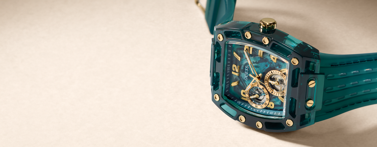 A luxury wristwatch with a translucent teal resin case and matching teal strap, featuring a skeleton dial with gold-tone details and gold-tone screws, set against a neutral beige background.