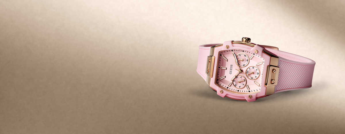 A pink watch with a pink textured strap, a rose gold-toned case, and a pink dial with white sub-dials, shown on a warm beige gradient background.