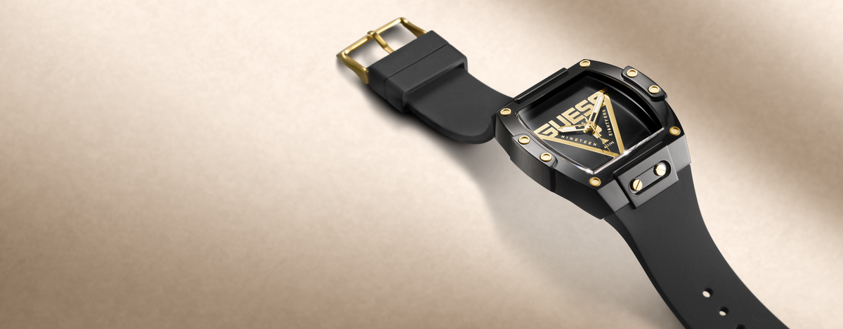 A luxury watch with a black rubber strap, a black ceramic case, and gold-tone accents on the dial and buckle, shown on a textured beige background.