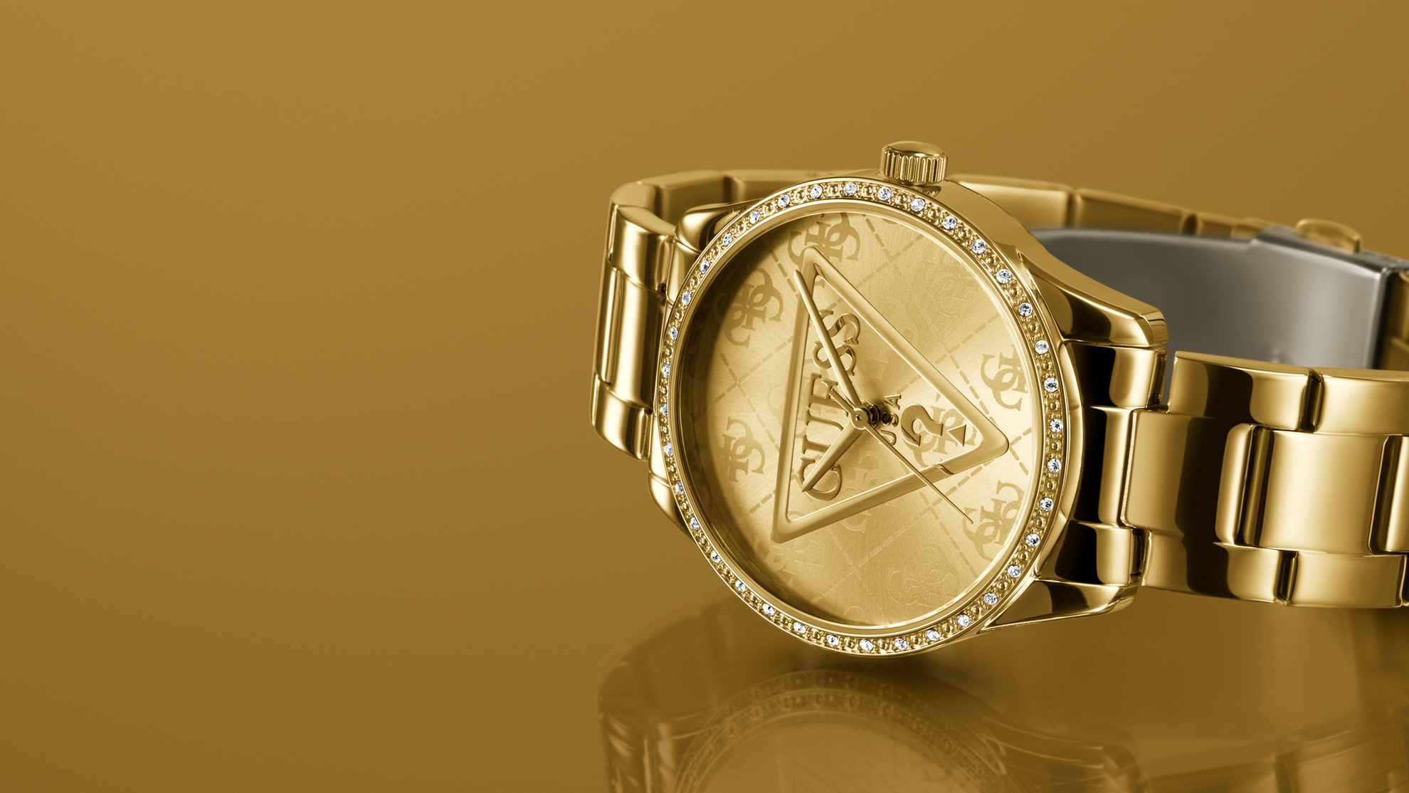 Gold watch with a triangle Guess brand logo on a reflective surface