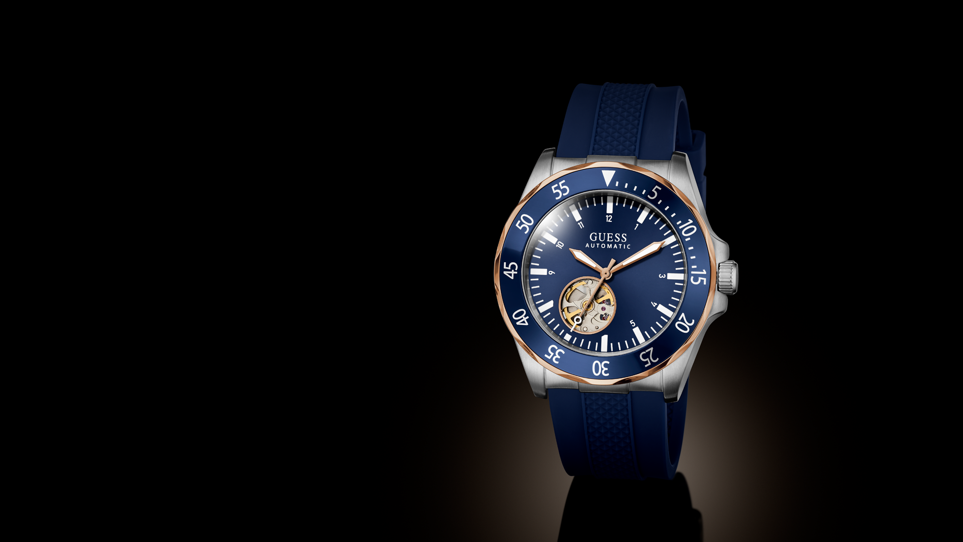 A Guess wristwatch with a blue dial, blue strap, and silver-tone case with a blue bezel, photographed on a black background with a spotlight effect.