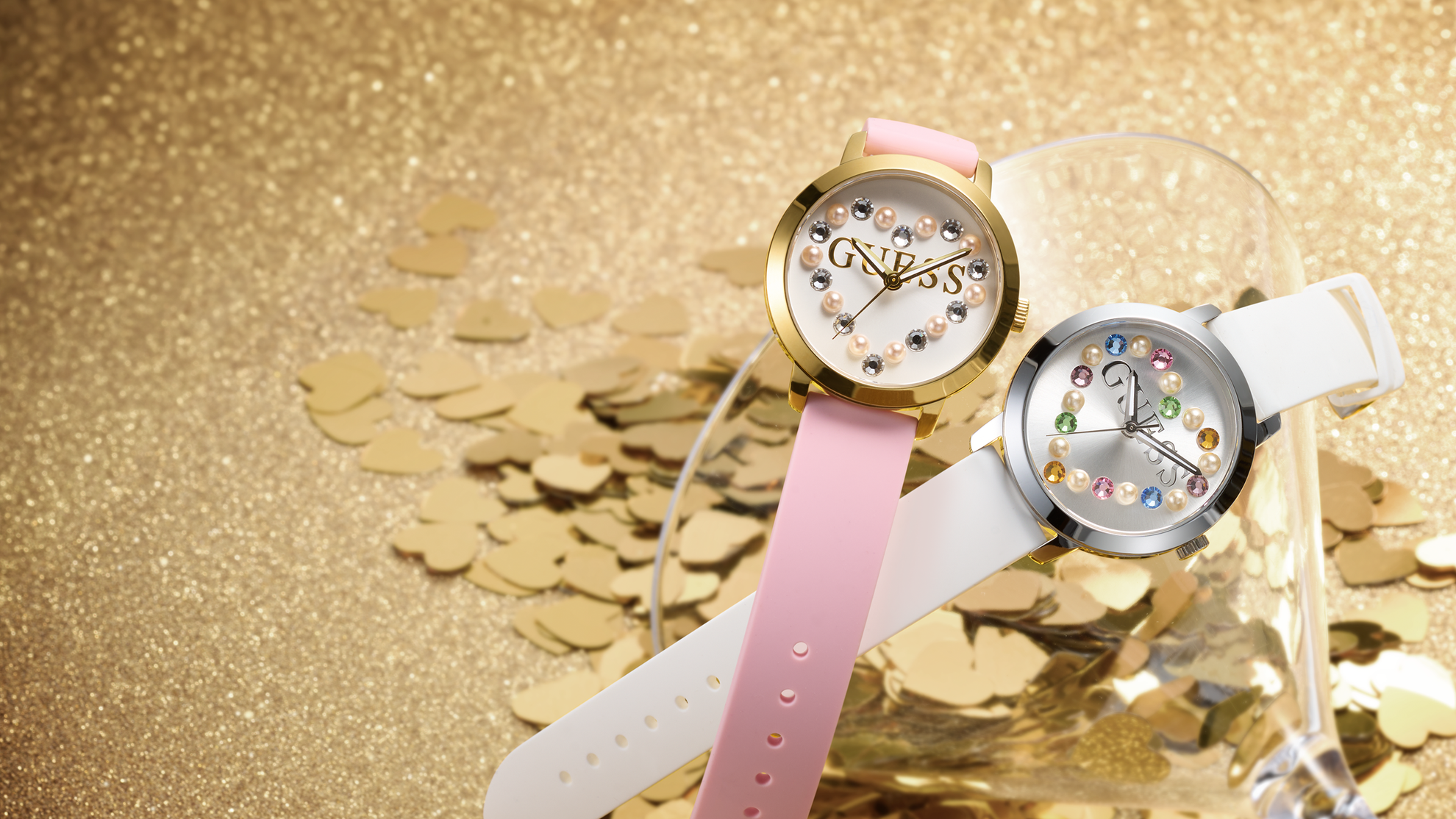 Two Womens GUESS watches with white and pink silicone straps lying on top of a martini glass