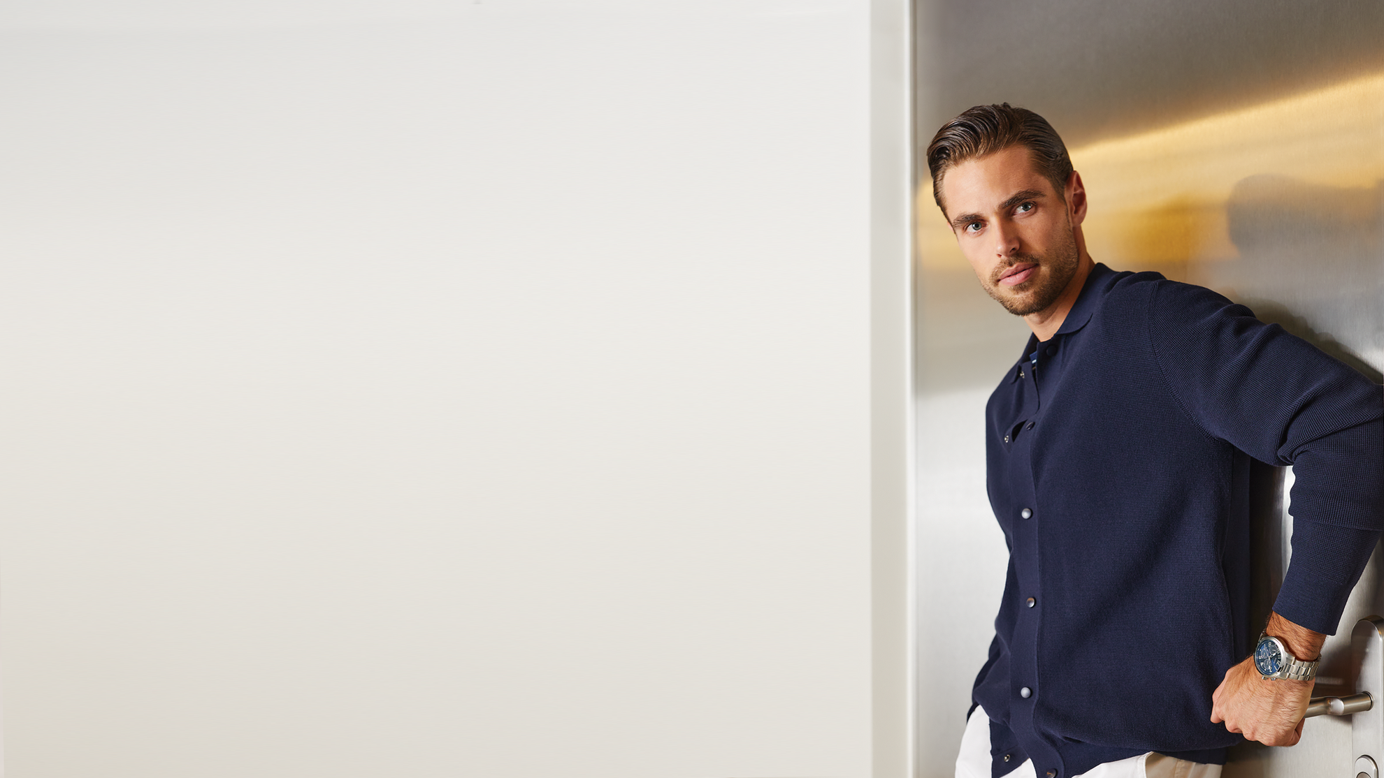 Man in a navy blue shirt leaning against a white wall with a light fixture.