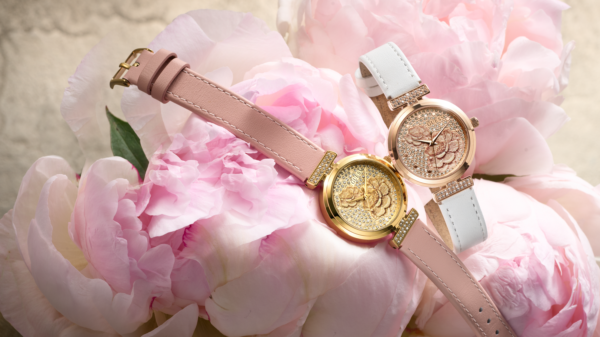 Two gold watches with pink and white straps on pink flowers