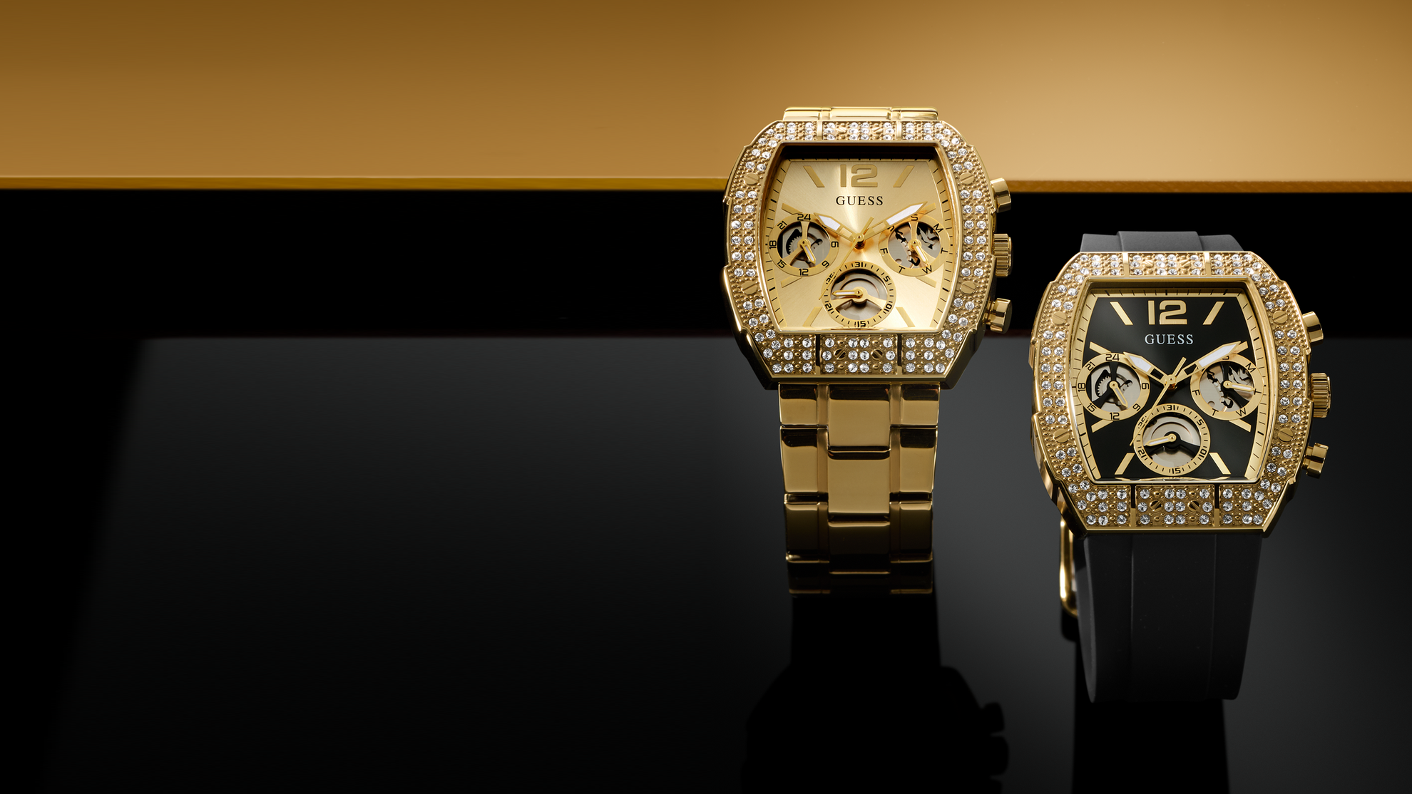 Two gold watches with diamond-studded faces on a reflective surface with a black and gold background.