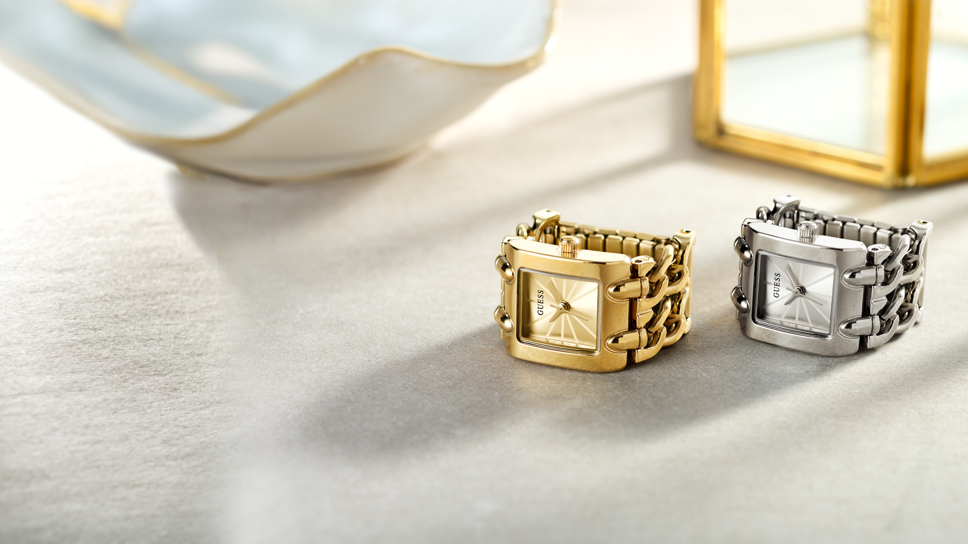 Two gold and silver square-shaped watch rings on a light surface.