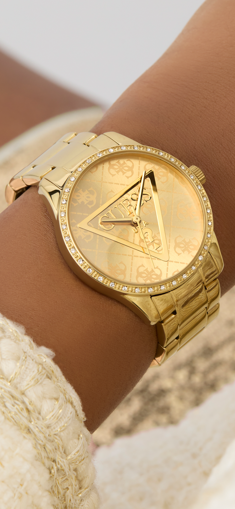 Gold watch with logo design on a wrist against a neutral background