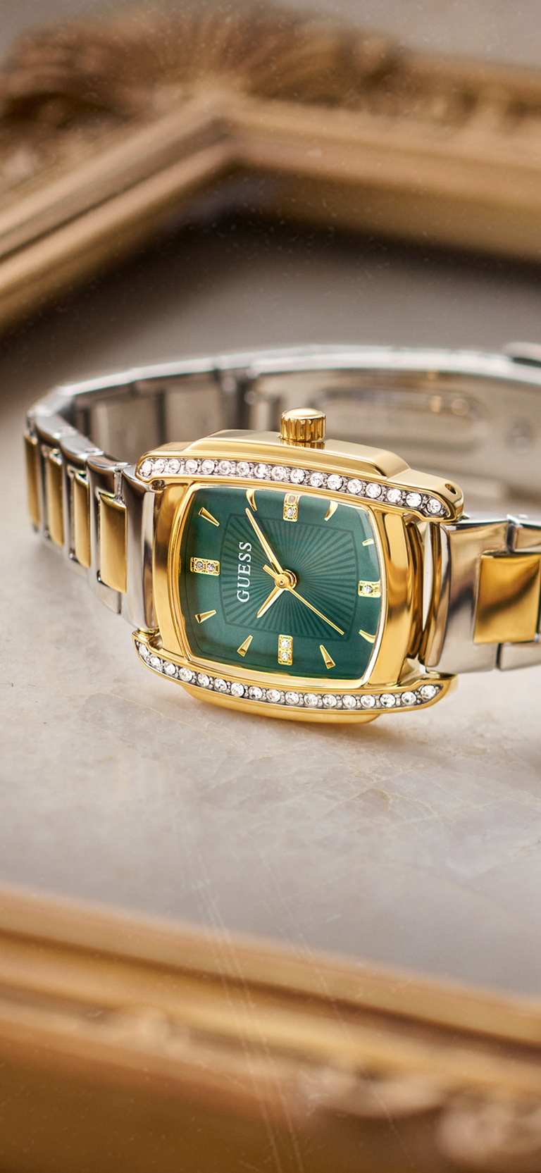 A Guess women's watch featuring a green dial, gold-tone case, and a two-tone silver and gold-tone metal link bracelet, accented with small clear crystals on the bezel.