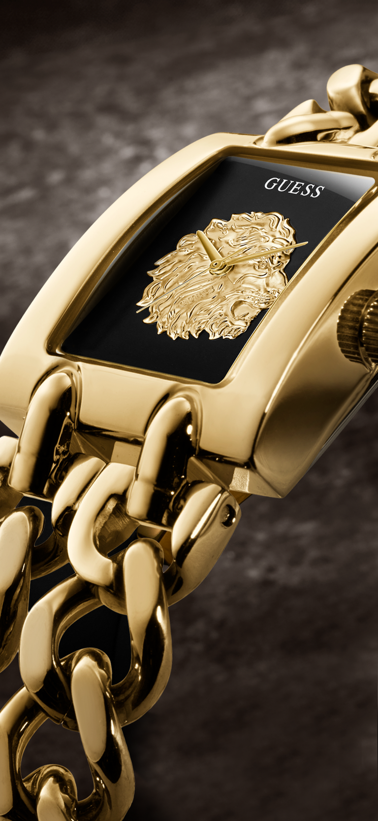 Close-up of a GUESS women's watch featuring a polished gold-tone case, a textured gold lion head dial, and a matching gold chain-link bracelet against a dark textured background.