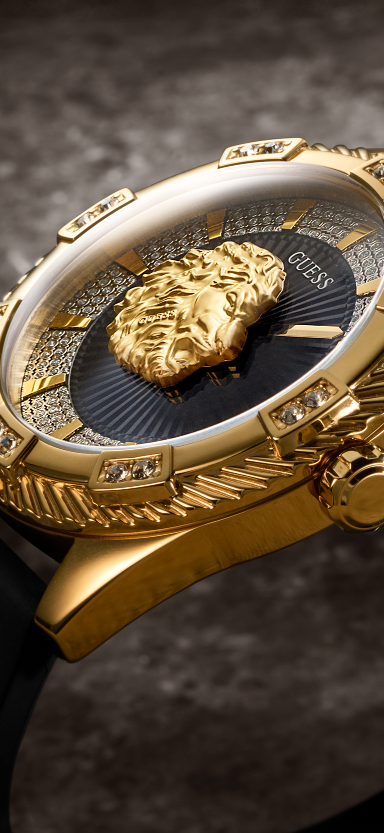 Close-up of a luxury wristwatch with a gold-tone case, a prominent gold lion head on the dark blue dial, and crystal accents, set against a dark textured background.