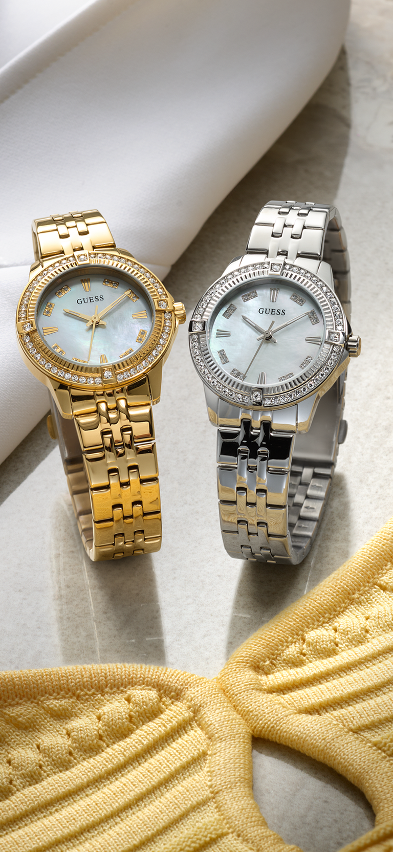 Two Guess watches, one gold and one silver, on a textured surface.