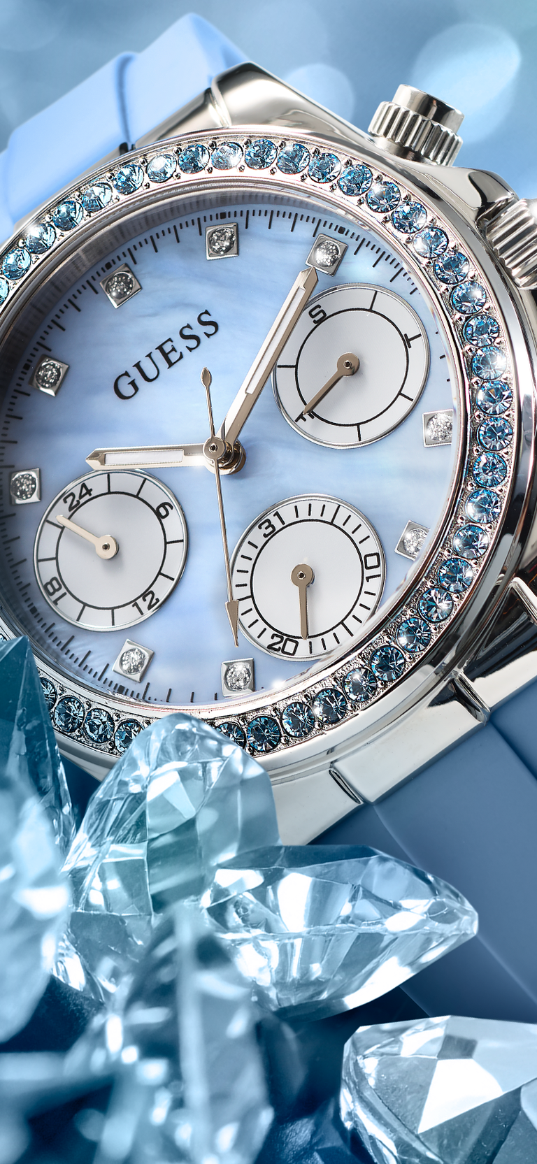 Silver GUESS Ladies Ice Blue Silver Tone Analog Watch with Swarovski ReCreated™ crystals with blue gemstones on a blue background
