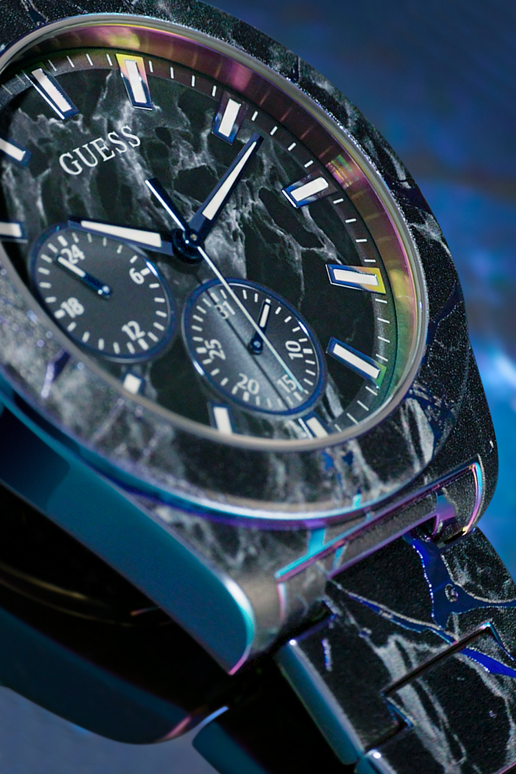 Close-up of a Guess watch with a black marble-like design on a blue gradient background