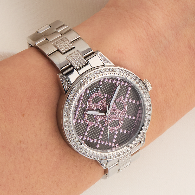 Silver Guess watch with a decorative face on a wrist against a neutral background