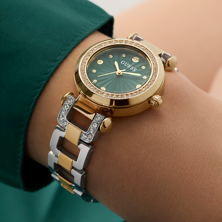 Gold and silver watch with green face on a wrist, brand 'Guess' visible