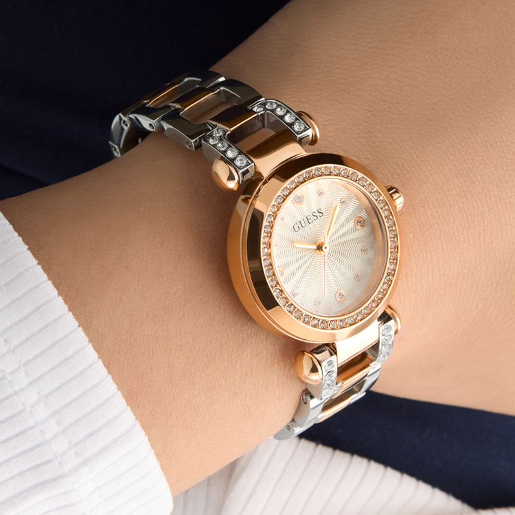 Rose gold and silver watch on a wrist with a blurred background