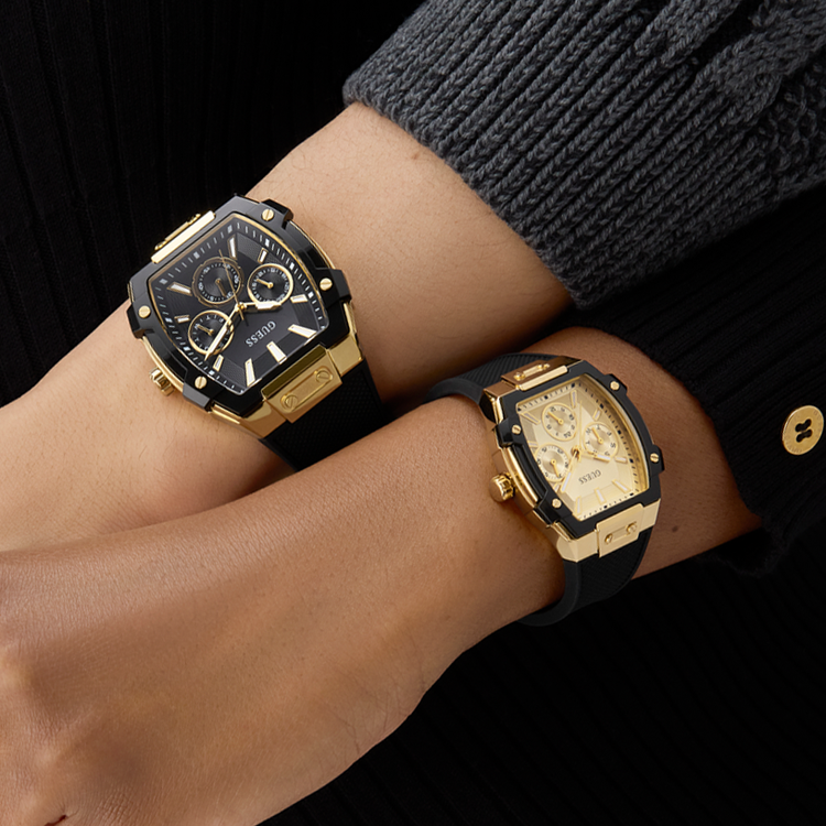 Two gold and black watches on a person's wrist against a dark background