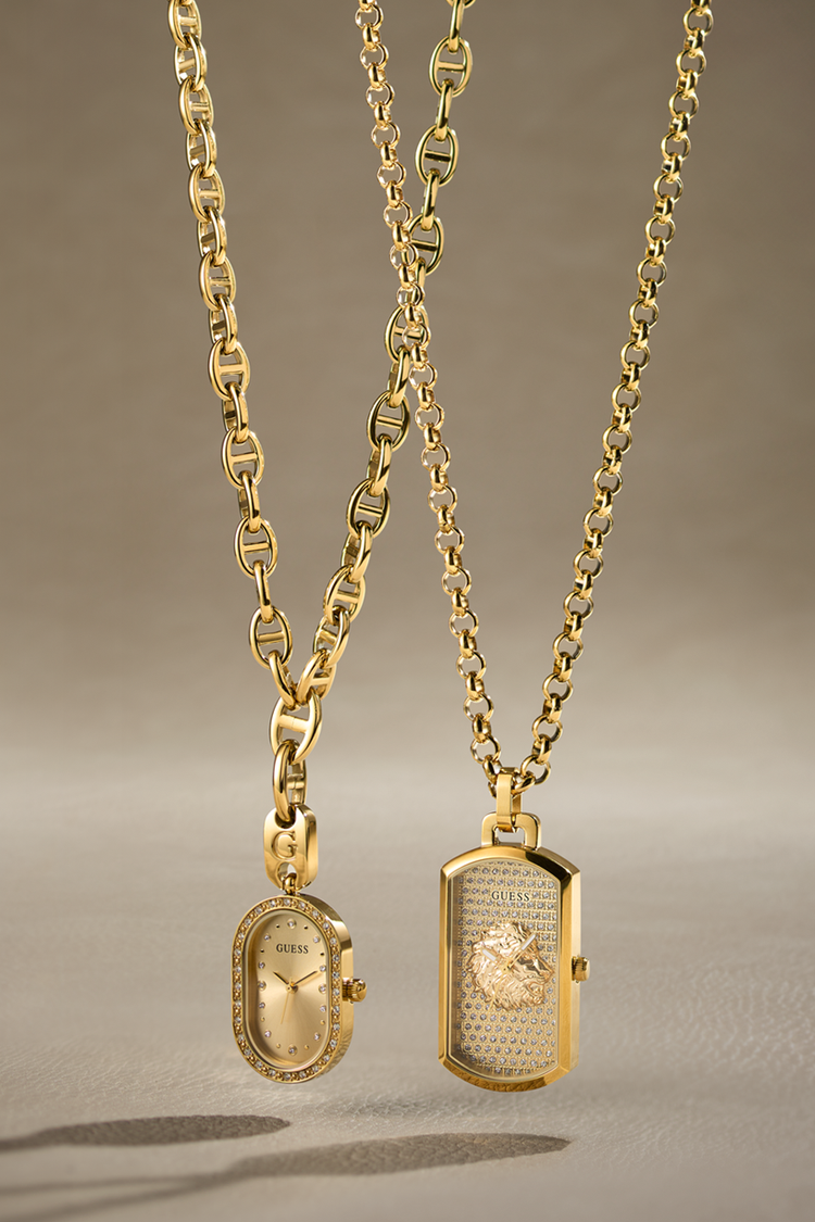 Two gold-tone pendant necklaces displayed against a neutral warm gray background. One necklace features an oval pendant with a vintage-style dial, and the other features a rectangular hinged box pendant with a textured center and a small round inset.