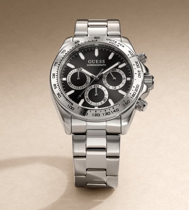 A stainless steel chronograph watch with a black dial and silver-tone metal bracelet, photographed on a clean beige background. The dial is branded GUESS.