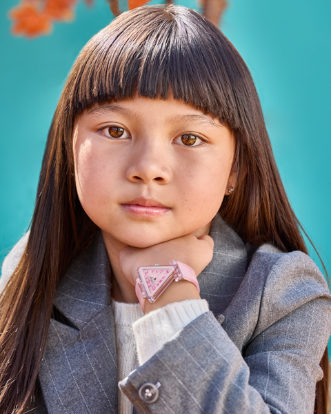 Young girl wearing a gray coat with a pink heart-shaped watch against a blue background