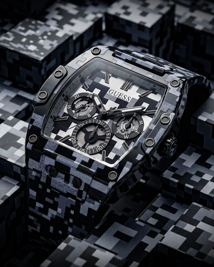 A GUESS wristwatch with a black and gray digital camouflage pattern, shown in a close-up product shot against a matching camouflage background.