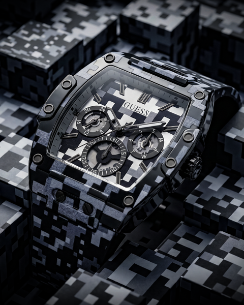 A GUESS wristwatch with a black and gray digital camouflage pattern, shown in a close-up product shot against a matching camouflage background.
