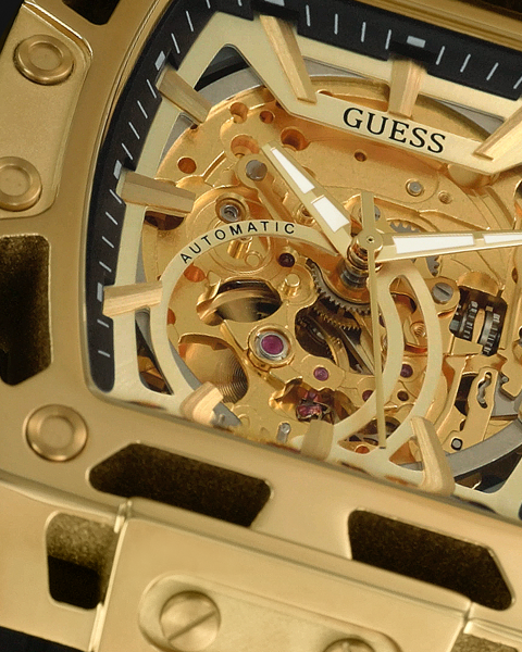 Close-up of an automatic gold watch with visible mechanical components and 'Guess' branding.