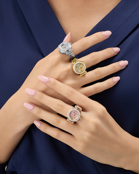 Close-up of a person's hands wearing three ornate rings with watch faces on a dark blue background.