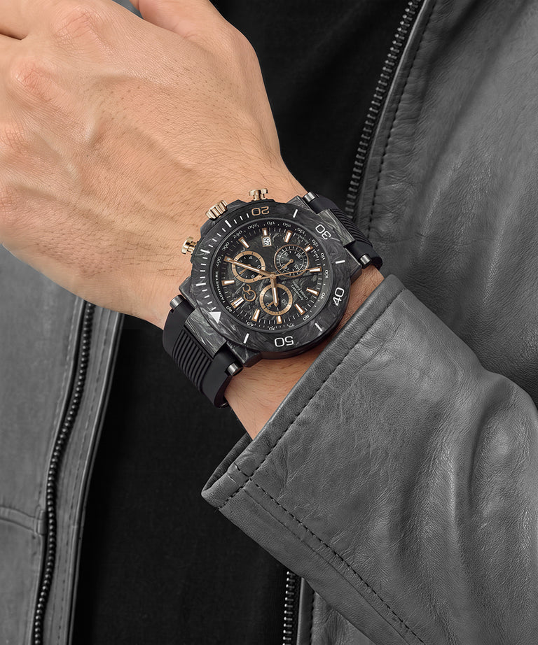 A close-up of a man's wrist wearing a black chronograph watch with gold-tone details, styled with a black shirt and a gray leather jacket.
