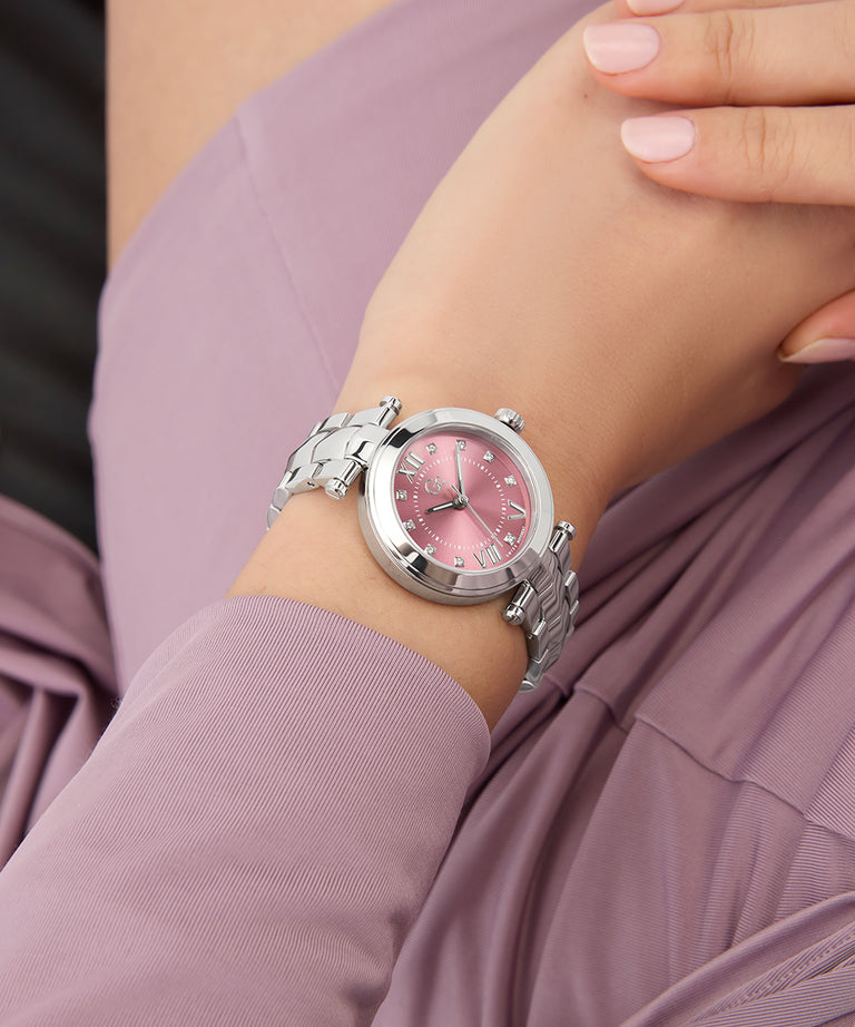 Pink Gc Illusion Small Size Metal watch with silver strap on a wrist, against a blurred pink background