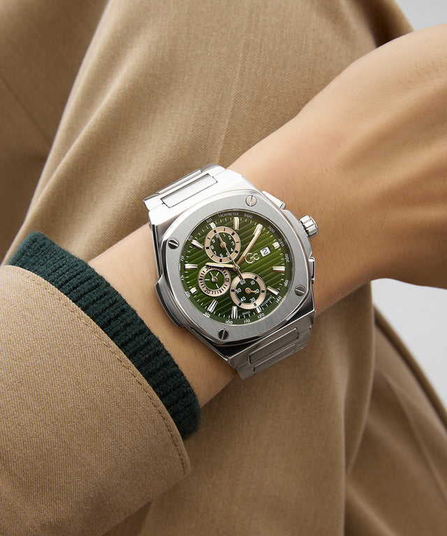 Gc Coussin Shape Chrono Metal Silver watch with a green face on a wrist, wearing a beige coat.