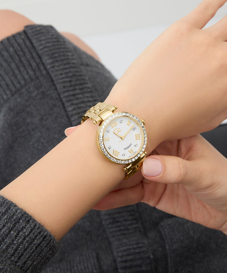 Gc Flair Crystal Mid Size Metal Gold wristwatch with a white face on a person's wrist, wearing a gray sweater.