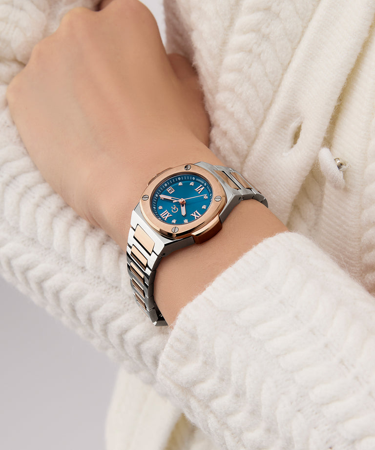 Wrist wearing a Gc Coussin Shape Mini Small Size Metal watch with a blue face against a white textured background