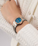 Wrist wearing a Gc Coussin Shape Mini Small Size Metal watch with a blue face against a white textured background
