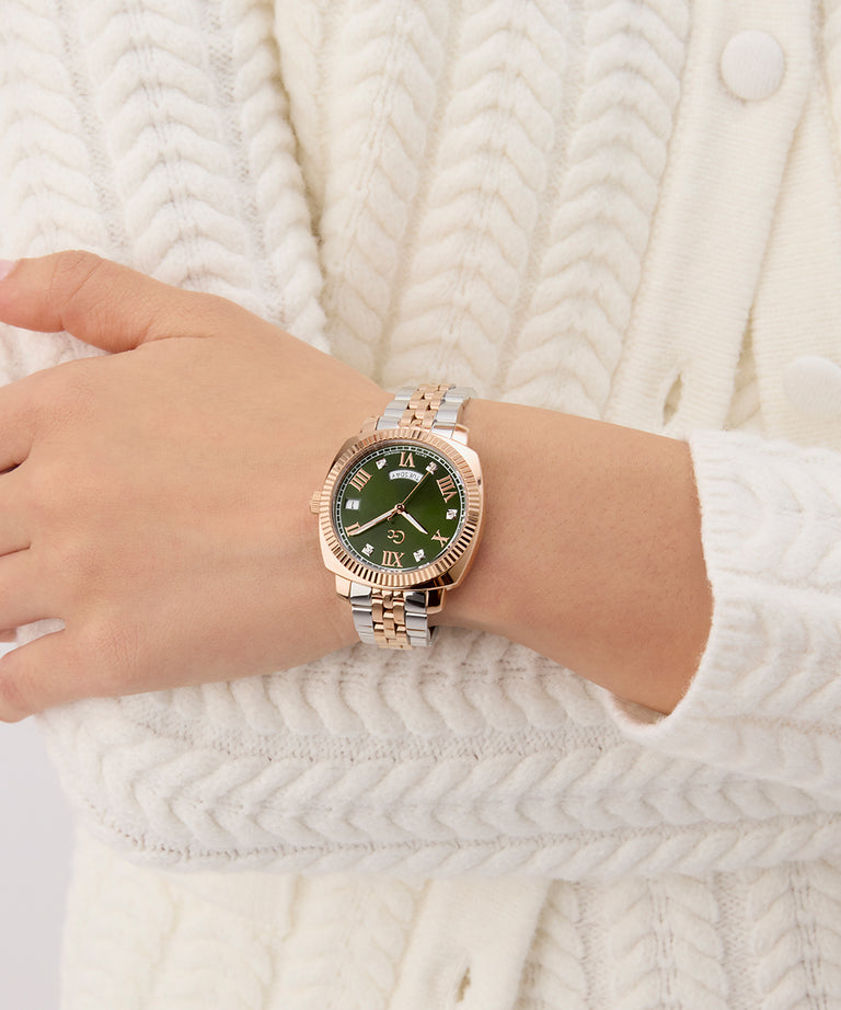 Hand wearing a Gc Flair Coussin Lady Mid Size Metal rose gold watch with a green face on a white textured background