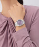 Woman wearing a silver Gc Flair Coussin Lady Mid Size Metal watch with a purple face on a light background
