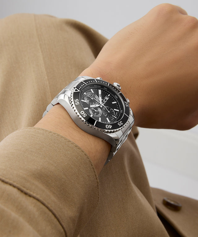 Close-up of a wrist wearing a Gc SpeedRacer Chrono Metal silver watch with a black face, against a neutral background.