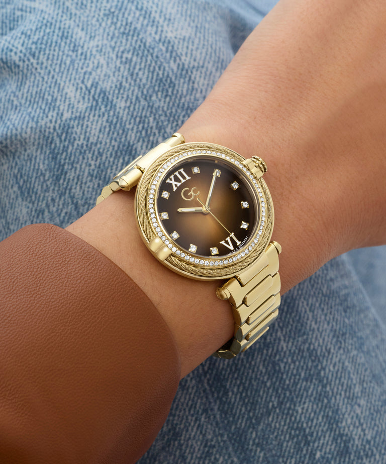 Gold Gc Vogue Cable Mid Size Metal wristwatch with black dial on a wrist against a denim background