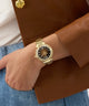 Gold Gc Vogue Cable Mid Size Metal watch on a wrist with a brown coat and blue jeans