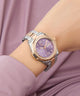 Gc Bolt Lady Mid Size Metal Watch with a purple face and silver and rose gold band on a person's wrist against a pink fabric background