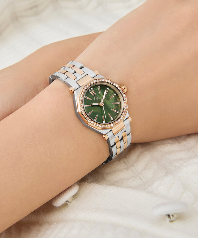 Wrist wearing a Gc Gleam Mini Small Size Metal silver and rose gold watch with a green face on a light background