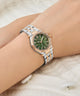 Wrist wearing a Gc Gleam Mini Small Size Metal silver and rose gold watch with a green face on a light background